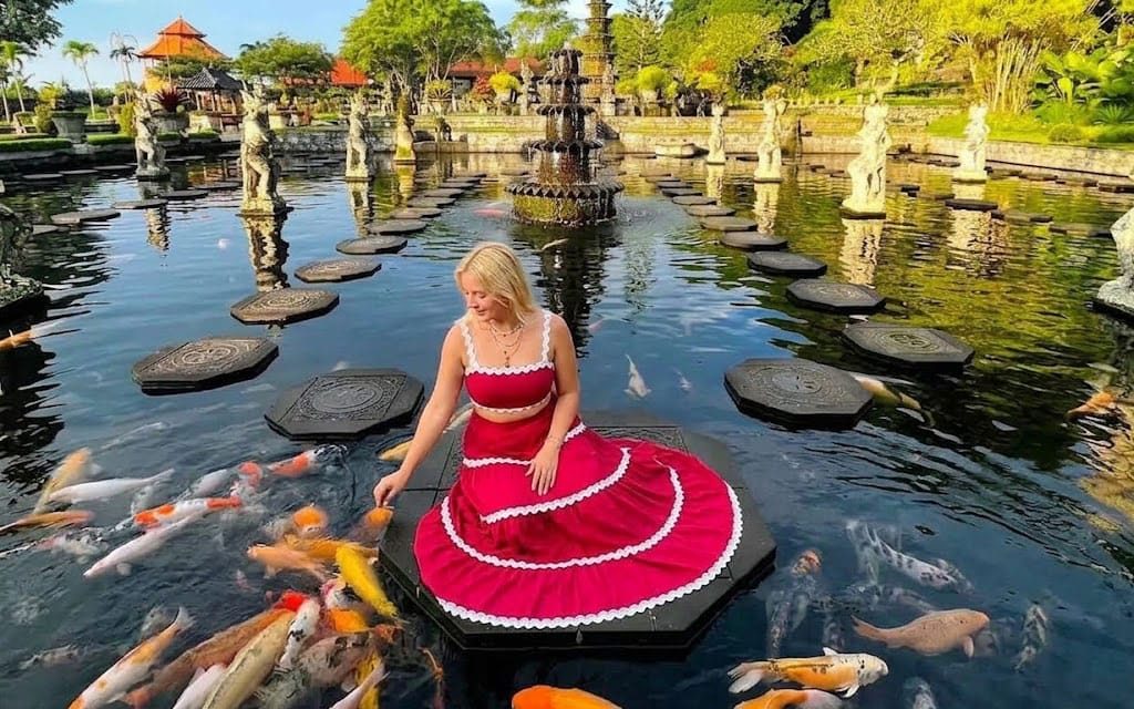 Woman relaxing on stepping stones surrounded by koi fish at Tirta Gangga, Bali.