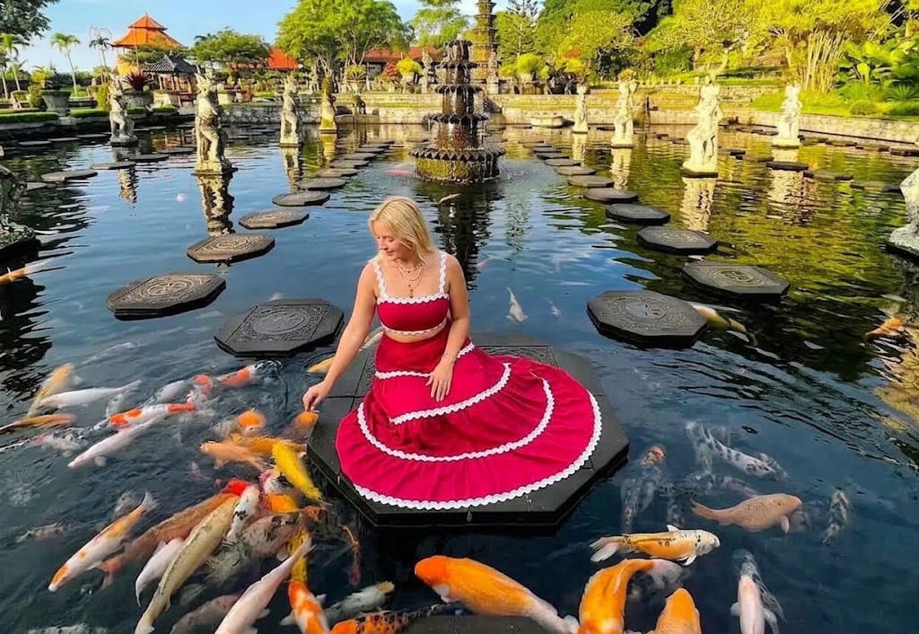 Woman relaxing on stepping stones surrounded by koi fish at Tirta Gangga, Bali.